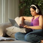 Student wearing headphone typing on laptop e-learning sitting on a couch at home