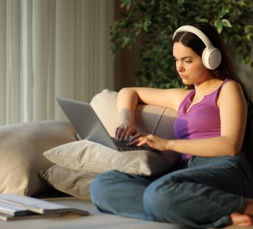 Student wearing headphone typing on laptop e-learning sitting on a couch at home